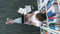 Studentin mit Laptop und Büchern in einer Bibliothek fotografiert von oben.